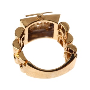 May include: A gold-toned ring with a watch face set into the band. The band is made of a series of linked squares.