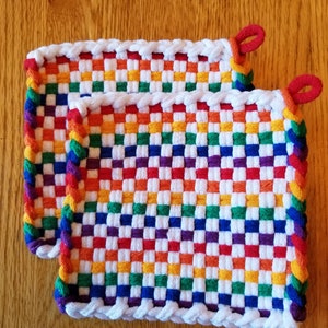 May include: Two rainbow coloured woven pot holders with white edging. The pot holders are made with a checkered pattern.