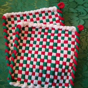 May include: Two woven potholders with a red, white, and green checkerboard pattern. The edges are trimmed with a white rope-like border and a red and green twisted cord. Each potholder has a red loop for hanging.