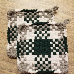 May include: Two woven pot holders in a green, white and grey checkered pattern. The pot holders have a loop on each corner.