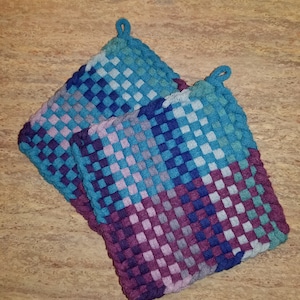 May include: Two woven pot holders in a blue, purple, and gray checkered pattern. The pot holders have a loop at the top for hanging.