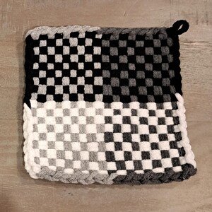 May include: A black and white checkered pot holder with a grey border and a loop for hanging.