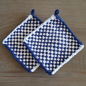 Puede incluir: Dos agarraderas de olla de tejido azul y blanco a cuadros con un lazo en cada esquina. Las agarraderas están hechas de tejido tejido y tienen un borde blanco.