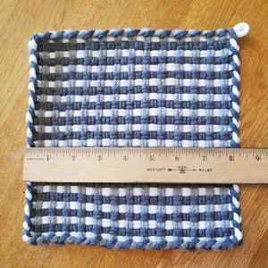 Może przedstawiać: Tkany podkładka pod gorące w kolorze szarym i białym z niebiesko-białym plecionym obrzeżem. Podkładka ma około 20 cm x 20 cm.