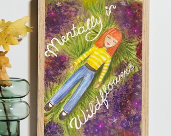 May include: A framed art print featuring a drawing of a person with orange hair lying in a field of purple and green wildflowers. The person wears a yellow and white striped long-sleeve shirt and blue jeans. The white text reads Mentally in Wildflowers.