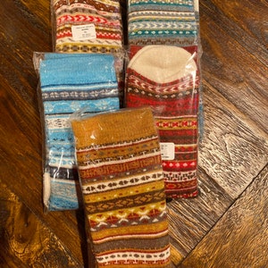 May include: Five pairs of colorful patterned socks in individual plastic packaging. The socks feature a variety of geometric and abstract designs in shades of blue, red, brown, and white.
