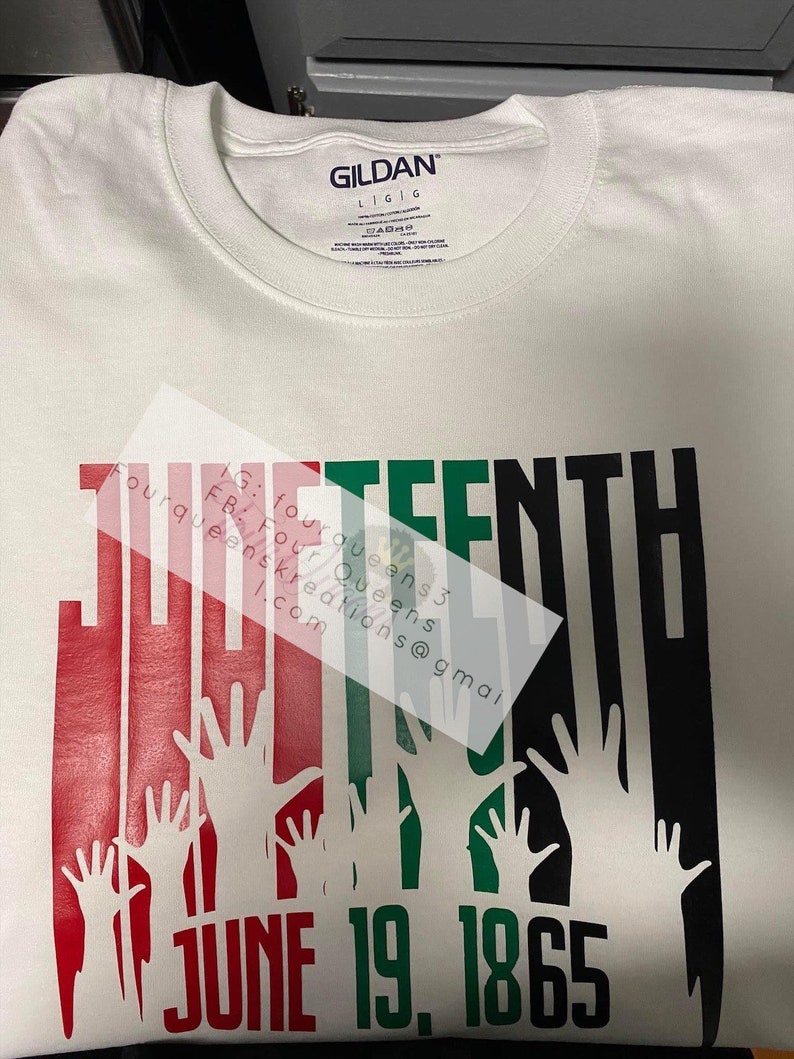 May include: White t-shirt with a graphic design featuring the word "THIRTEENTH" in red, green, and black, with raised hands and the date "JUNE 19, 1865". The shirt has a crew neck and the Gildan brand label.