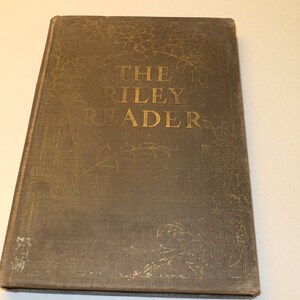 May include: The cover of a vintage book titled "The Riley Reader". The cover is a dark brown with gold lettering and decorative floral designs.