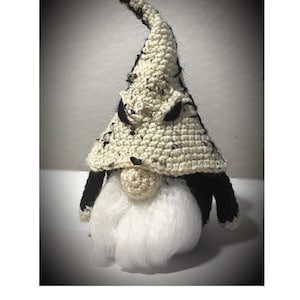 May include: A crocheted gnome with a white and black hat. The hat has a pointed top and a black trim around the brim. The gnome has a white beard and a black nose.