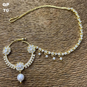 May include: Gold nose ring with a chain and pearl accents. The ring is decorated with clear rhinestones and has a floral design. The chain is also decorated with clear rhinestones and has a pearl drop at the end.