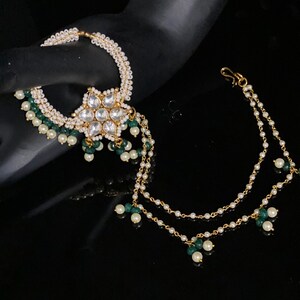 May include: A gold nose ring with a white flower design and green and white beads. The ring is attached to a chain with green and white beads.