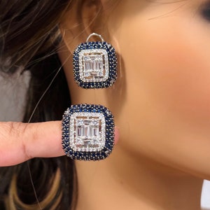 Può includere: Un paio di orecchini d'argento e un anello con un design quadrato. Gli orecchini e l'anello sono incastonati con pietre trasparenti a forma di baguette e pietre rotonde blu.