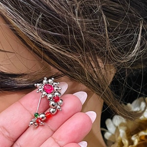 Puede incluir: Anillo de nariz de plata con cuentas rojas y verdes y una gema rosa.