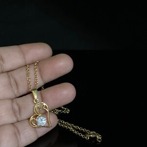 May include: A gold chain necklace with a heart-shaped pendant featuring a clear rhinestone in the center.