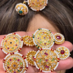 May include: A set of gold-toned jewellery with white and red stones. The jewellery includes a necklace, earrings, and a headpiece.