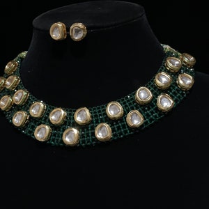 May include: A green and gold choker necklace with large, clear, faceted stones. The necklace is on a black velvet display stand. Matching earrings are also included.
