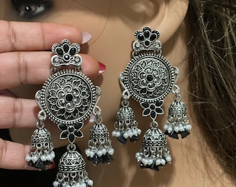May include: Silver earrings with black and white beads. The earrings feature a round, ornate design with a black stone in the center. The earrings are dangling and have a bell-shaped design.