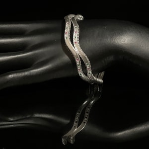 May include: Three silver bangles with a wavy design and small red and green gemstones.