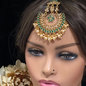 May include: Gold and green jeweled headpiece with a pearl drop design. The headpiece is a traditional Indian style accessory.