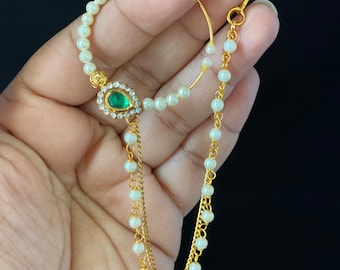 May include: A gold nose ring with a green gem and a pearl chain. The ring is attached to a double chain with pearls.