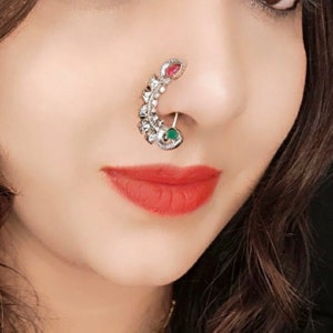 May include: A silver nose ring with a green and pink stone design. The ring is curved and has intricate details.