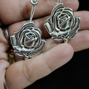 May include: A pair of silver earrings with a rose design. The roses are detailed and have a vintage look.