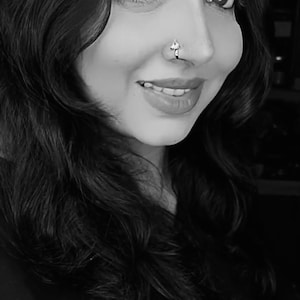 May include: A black and white portrait of a person with long dark hair. The person is wearing a nose ring.