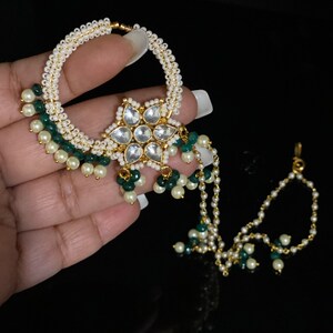 May include: A gold nose ring with a star-shaped pendant adorned with white stones and green beads. The ring is attached to a chain with white and green beads.