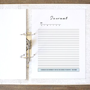 May include: A white binder with a blank page on the left and a page with the word "Journal" and lined paper on the right. The page also has the text "Journaling is whispering to ones self and listening at the same time." -  Anna Plummer