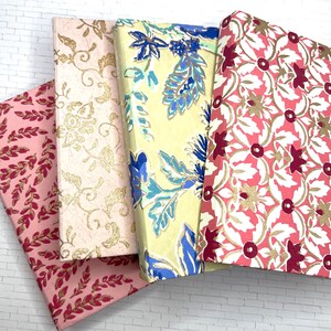 May include: Four small notebooks with different floral patterns. The covers are pink, yellow, and white with gold accents. The notebooks are stacked on top of each other.