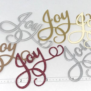May include: Assortment of die-cut "Joy" word cutouts in various colors, including silver, gold, cream, brown, and red glitter. The cursive font adds a decorative touch, suitable for crafts and holiday projects.