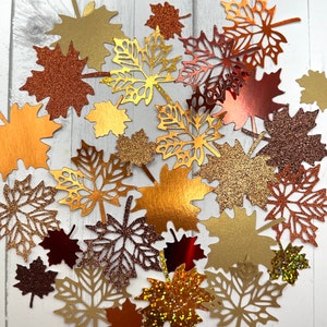 May include: A collection of fall-themed paper leaves in various shades of brown, gold, and red. The leaves are decorated with glitter and have a variety of shapes and sizes.