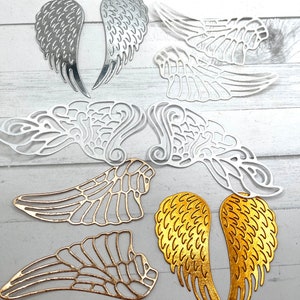 May include: A collection of metal angel wing cutouts in various colors, including silver, gold, and bronze. The wings feature intricate designs and textures, perfect for crafting or decorative projects. The wings vary in size and style.