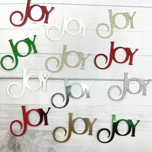 May include: Twelve paper cutouts of the word "joy" in various colors and finishes, including red, green, gold, silver, and white. Some of the cutouts have glitter.
