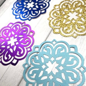 May include: Four decorative paper cutouts in the shape of a mandala. The cutouts are in blue, gold, purple, and light blue.