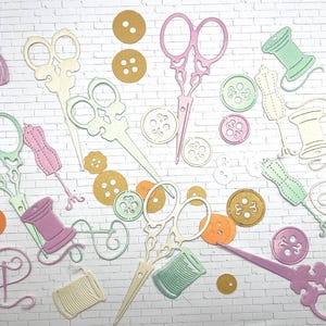 May include: A collection of pastel-colored sewing-themed cutouts scattered on a white brick background. The image includes scissors, spools of thread, buttons, and dress forms in shades of pink, green, yellow, and cream. The items are arranged in a visually appealing, scattered pattern.