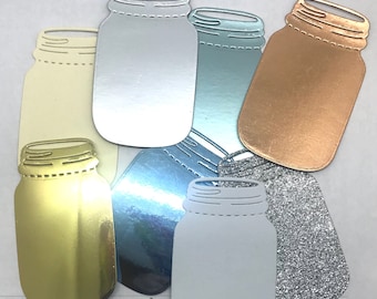May include: A collection of metallic mason jar cutouts in various colors, including gold, silver, and copper. The jars are arranged in a scattered pattern, with a glittery silver jar at the bottom right. The cutouts are likely for crafting or decorative purposes.