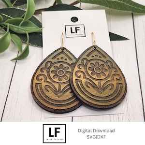 May include: A pair of wooden teardrop earrings with a floral design. The earrings are laser-cut with a detailed flower and stem pattern. The wood has a gradient of gold and brown tones, and the earrings hang from gold-colored hooks.