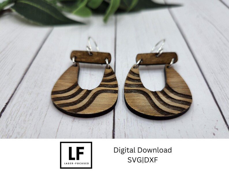 May include: A pair of wooden earrings with a wavy pattern. The earrings are brown with black lines and have a simple hoop design. The earrings are shown on a white surface.