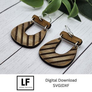 May include: A pair of wooden earrings with a striped pattern. The earrings are shaped like a teardrop with a cutout in the middle. The earrings are hanging from silver hooks.