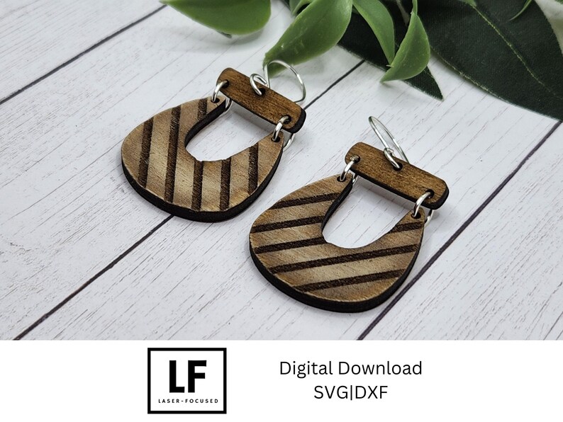 May include: A pair of wooden earrings with a striped pattern. The earrings are shaped like a teardrop with a cutout in the middle. The earrings are hanging from silver hooks.