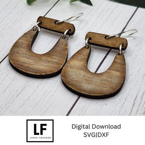 May include: A pair of wooden earrings with a U-shaped design. The earrings are a light brown colour and have a natural wood grain finish.