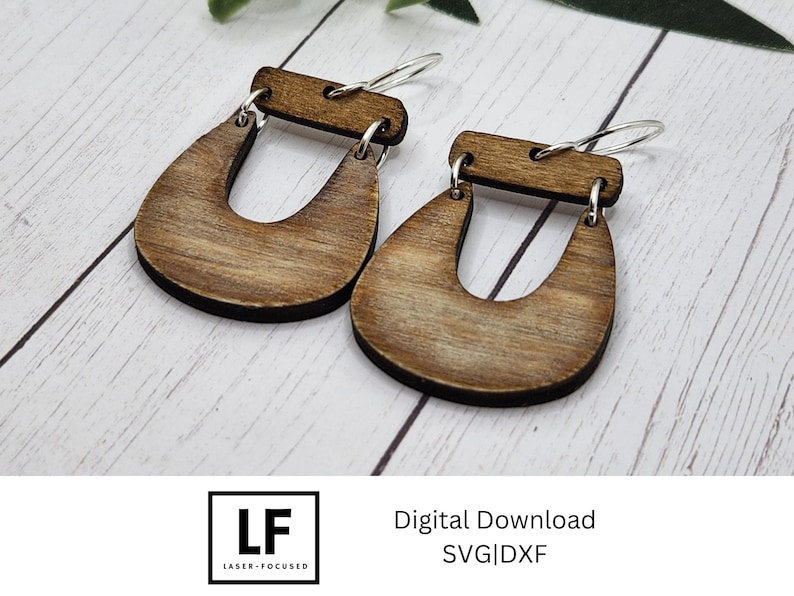 May include: A pair of wooden earrings with a U-shaped design. The earrings are a light brown colour and have a natural wood grain finish.