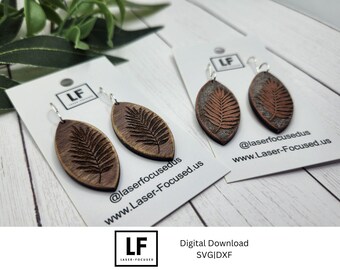 May include: Wooden leaf-shaped earrings with a fern design, displayed on white cards. The earrings are brown with a darker brown fern pattern. The cards have the text "@laserfocusedus" and "www.Laser-Focused.us".