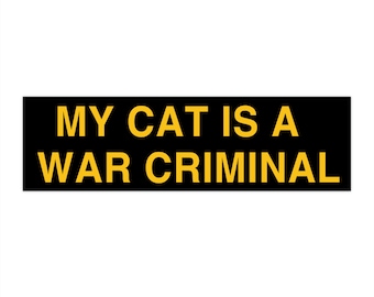 May include: Black and yellow rectangular sign with the text "MY CAT IS A WAR CRIMINAL" in yellow letters.