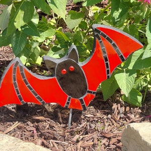 May include: A red and black mosaic bat garden stake. The bat has large, round eyes and is made of glass tiles.