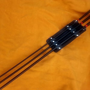 Puede incluir: Cuatro varillas de metal negro con puntas rojas están aseguradas en una funda de cuero negro con remaches plateados.