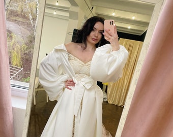 May include: A white satin dress with a long skirt and a fitted bodice. The dress has a large, puffy collar and long sleeves. The dress is tied at the waist with a white satin sash.