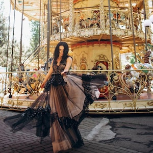 May include: A floor-length sleeveless dress featuring a black lace bodice with a deep V-neckline and a voluminous, layered tulle skirt in black and beige, accented with black sequin embellishments along the hem and waistline.