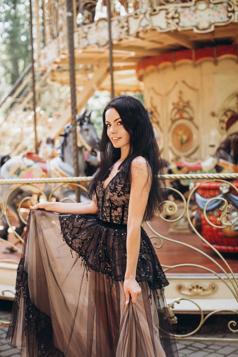 May include: A floor-length dress featuring a black lace bodice with a deep V-neckline over a nude-colored lining. The skirt consists of a layered black tulle overlay with sequin embellishments and a solid black waistband, creating a full silhouette.
